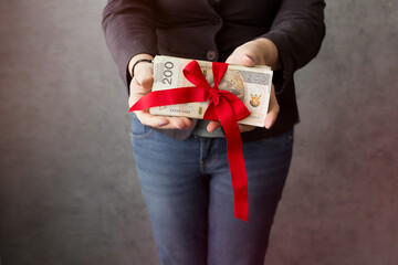 Kobieta trzyma w rękach dużo polskich pieniędzy przewiązanych czerwoną wstążką