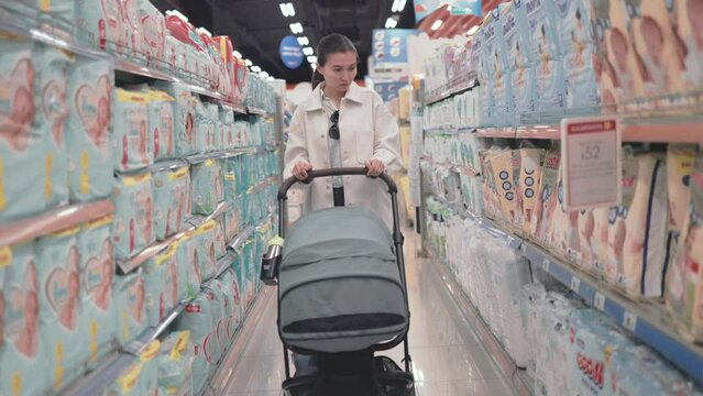Woman push a stroller between diapers rows in supermarket 