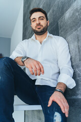 Vertical image of handsome bearded man, businessman in fashion and trendy outfit, looking at camera. Low angle view