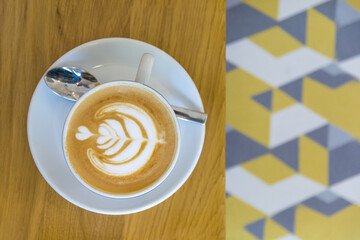 Beautiful cappuccino with latte art on wooden table in small town cafeteria