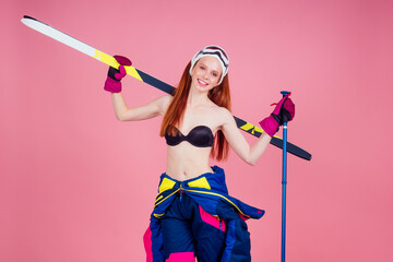 Attractive smiling young redhaired ginger woman skier in sunglasses, bikini and flower posing with...