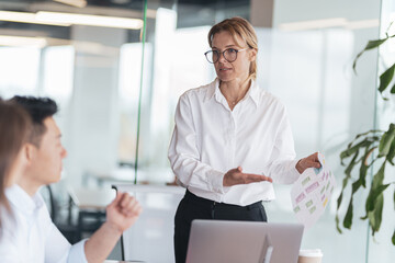 Business mature woman talking on presentation financial statistics at briefing in office.