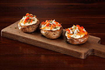 Baked potatoes stuffed with melted cheese with mayonnaise, grated carrots and bell peppers on a cutting board. Close-up. View from an angle.