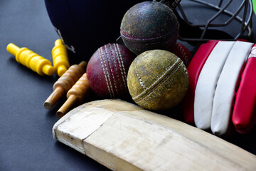 Old training cricket sport equipments on dark floor, leather ball, wickets, helmet and wooden bat, soft and selective focus, traditional cricket sport lovers around the world concept.