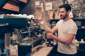 Caucasian happy male bartender making coffee at professional machine. Work in cafeteria. Cafe worker