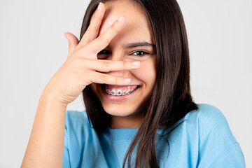 Ashamed and funny teen girl with braces covering face with hand.