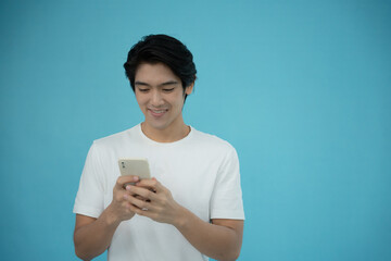 Handsome Asian man smiling happy with his phone on light blue background.