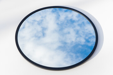 A round or oval mirror with a reflection of the blue sky and white clouds. Close-up. Isolated on a white background