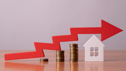 Coins on a table, a red up arrow and house. The concept of the rising price of real estate