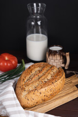Fresh homemade rye bread, tomato, bunch onion, clay mug and bottle of milk on wooden cutting board