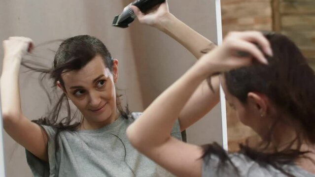 Woman brunette hairdresser shaves hair with a machine for haircut, standing near the mirror and talking. Beautiful woman shaves hair with a trimmer bald. Concept of hairstyle.