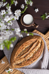 Obraz na płótnie Canvas Fresh homemade rye cereal bread with clay mug of milk on wooden cutting board. Healthy breakfast