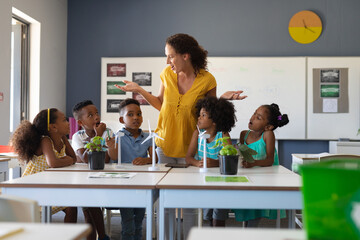 Surprised caucasian female teacher looking at african american elementary students at desk in class