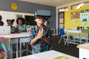 Smiling african american elementary schoolboy wearing vr glasses while standing in classroom