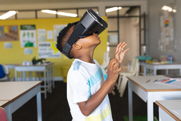 Side view of african american elementary schoolboy gesturing while wearing vr glasses in classroom - Powered by Adobe