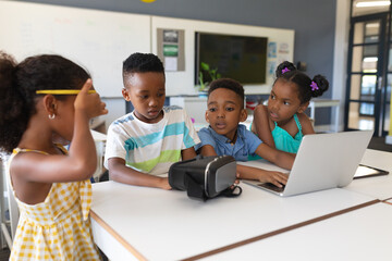 African american elementary school students using vr glasses and laptop at desk in classroom