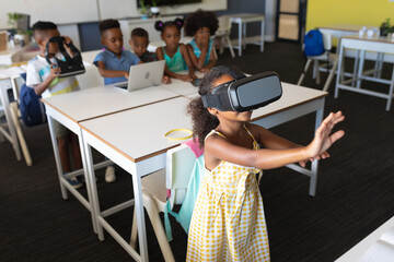 African american elementary schoolgirl gesturing while wearing vr glasses in classroom