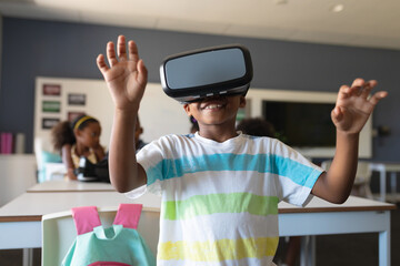 Smiling african american elementary schoolboy gesturing while wearing vr glasses in classroom