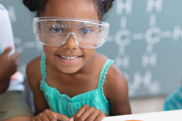 Portrait of smiling african american elementary schoolgirl wearing protective eyewear in laboratory - Powered by Adobe