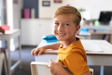 Portrait of smiling caucasian elementary schoolboy sitting at desk in classroom