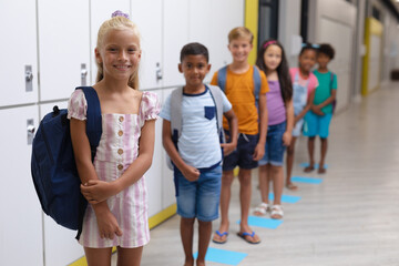 Portrait of smiling multiracial elementary school students standing in row by lockers in corridor
