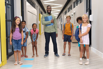 Portrait of cheerful african american young male teacher with multiracial elementary students