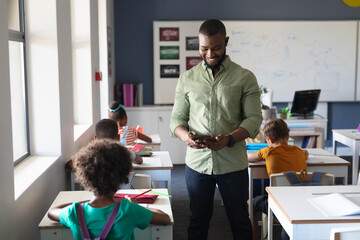 African american young male teacher using digital tablet while standing by multiracial students