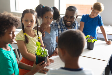 African american young male teacher and multiracial elementary students discussing over plants