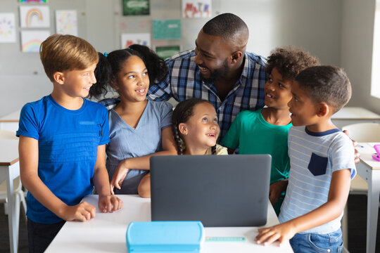 Happy african american young male teacher with multiracial elementary students using laptop
