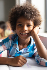 Portrait of smiling african american elementary boy with curly hair sitting at desk in classroom