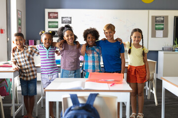 Portrait of smiling multiracial elementary school students standing with arm around in classroom