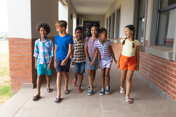 Full length of smiling multiracial elementary school students walking in school corridor