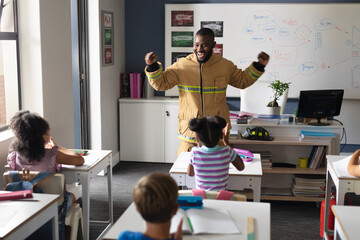 African american young male teacher in firefighter uniform with multiracial elementary students