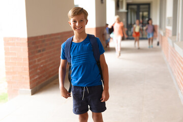Portrait of smiling caucasian elementary schoolboy standing in corridor