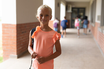 Portrait of smiling caucasian elementary schoolgirl standing in corridor
