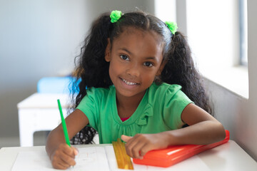 Portrait of smiling african american elementary schoolgirl with ponytails sitting at desk in class