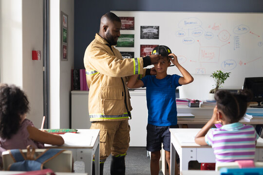African american young male teacher wearing protective helmet to caucasian elementary boy in class