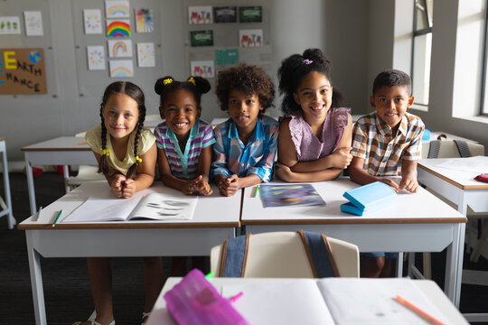 Smiling multiracial elementary school students sitting at desk in classroom