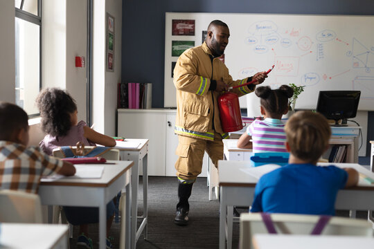 African american young male teacher in uniform teaching fire extinguisher to multiracial students