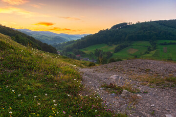 mountainous countryside landscape at dawn. rural fields on the hills. village in the distant valley. gorgeous sky with clouds glowing in morning light