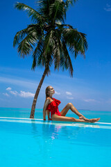 Elegant tanned woman in red swimsuit in pool on tropical Maldives island. Beautiful bikini girl in pool with view on horizon. Sexy model near the pool on beautiful Indian ocean landscape. Travel. 