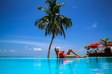 Fototapeta na wymiar Elegant tanned woman in red swimsuit in pool on tropical Maldives island. Beautiful bikini girl in pool with view on horizon. Sexy model near the pool on beautiful Indian ocean landscape. Travel. 