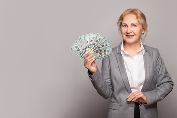 Senior business woman showing money us dollars on gray background