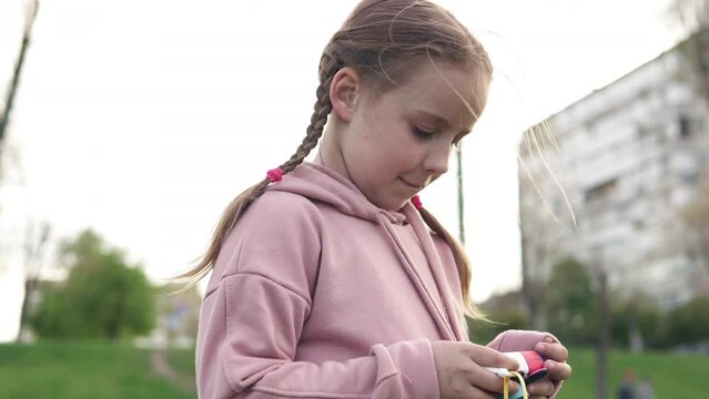 A little girl photographer in nature looks at the footage on a children's camera.