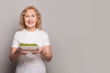 Happy senior woman holding microgreen vegetarian food on gray studio wall banner background