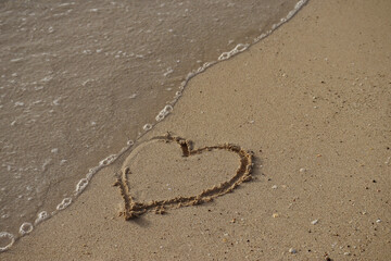 Fototapeta na wymiar A wave washes away a heart drawn in the sand