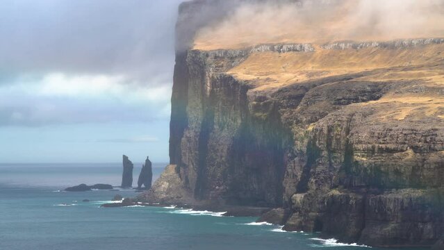 Panorama view of beautiful rainbow shining in front of massive coastline and Risin og Kellingin sea stacks, in background Streymoy Island, Faroe Islands