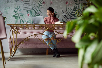A happy multicultural female student using the laptop for e-learning in a coffee shop.
