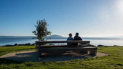 Naklejka na ściany i meble Couple sitting on the bench by the Rotorua lakefront, Rotorua.