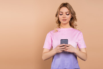 woman with wavy hair messaging on smartphone isolated on beige.